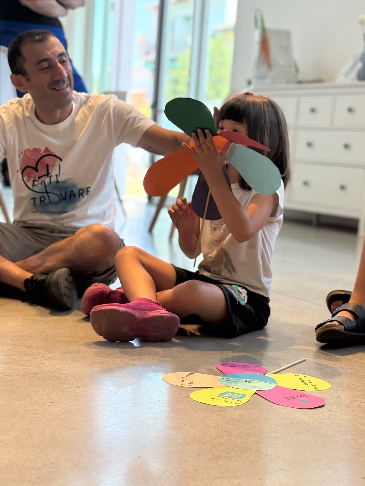 Una bambina guarda un grande fiore di carta colorata accanto a un uomo che le sorride