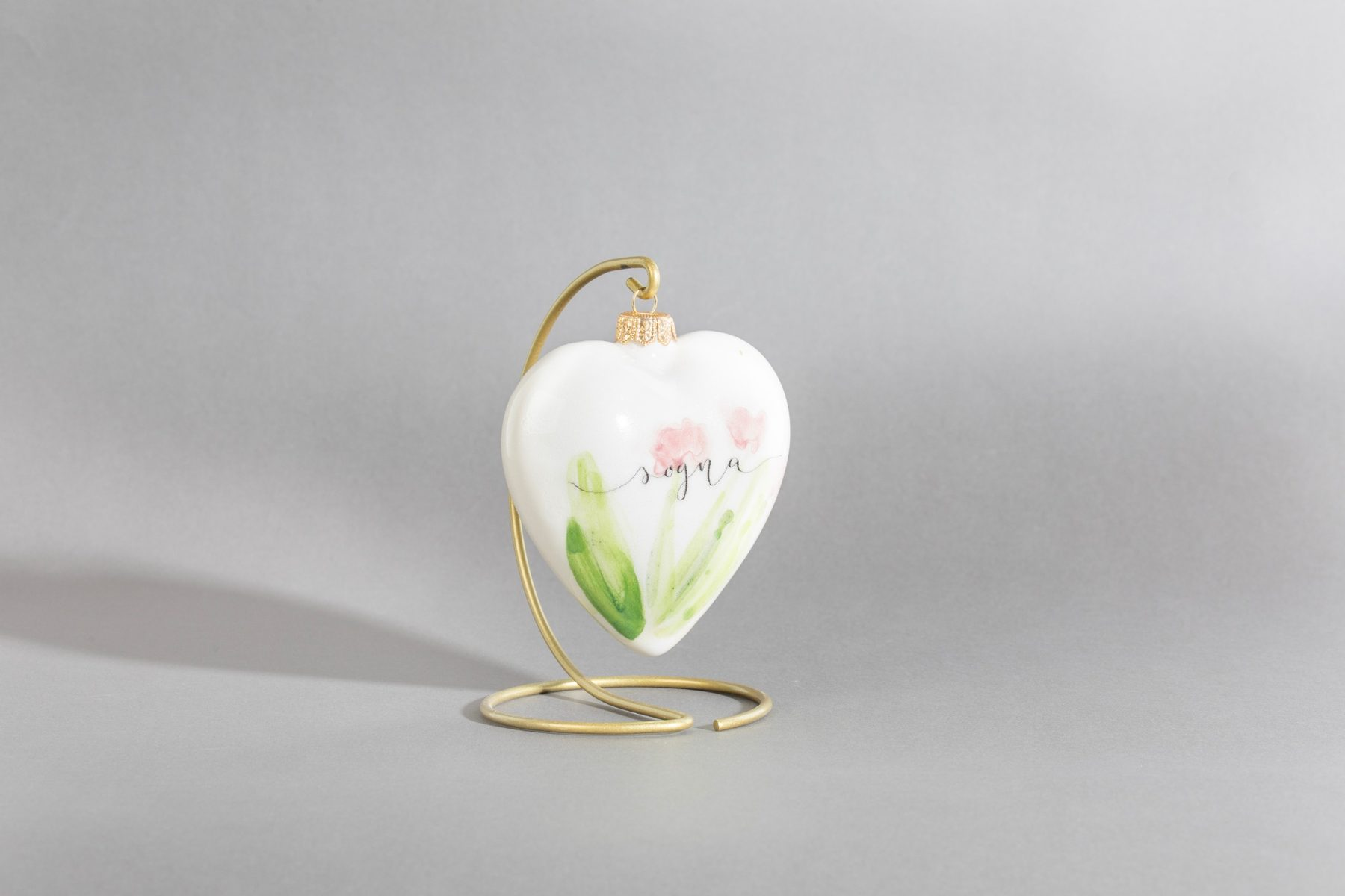 Un Desiderio, decorazione natalizia a cuore in ceramica bianca dipinta a mano con fiori rosa e la scritta sogna, su supporto dorato