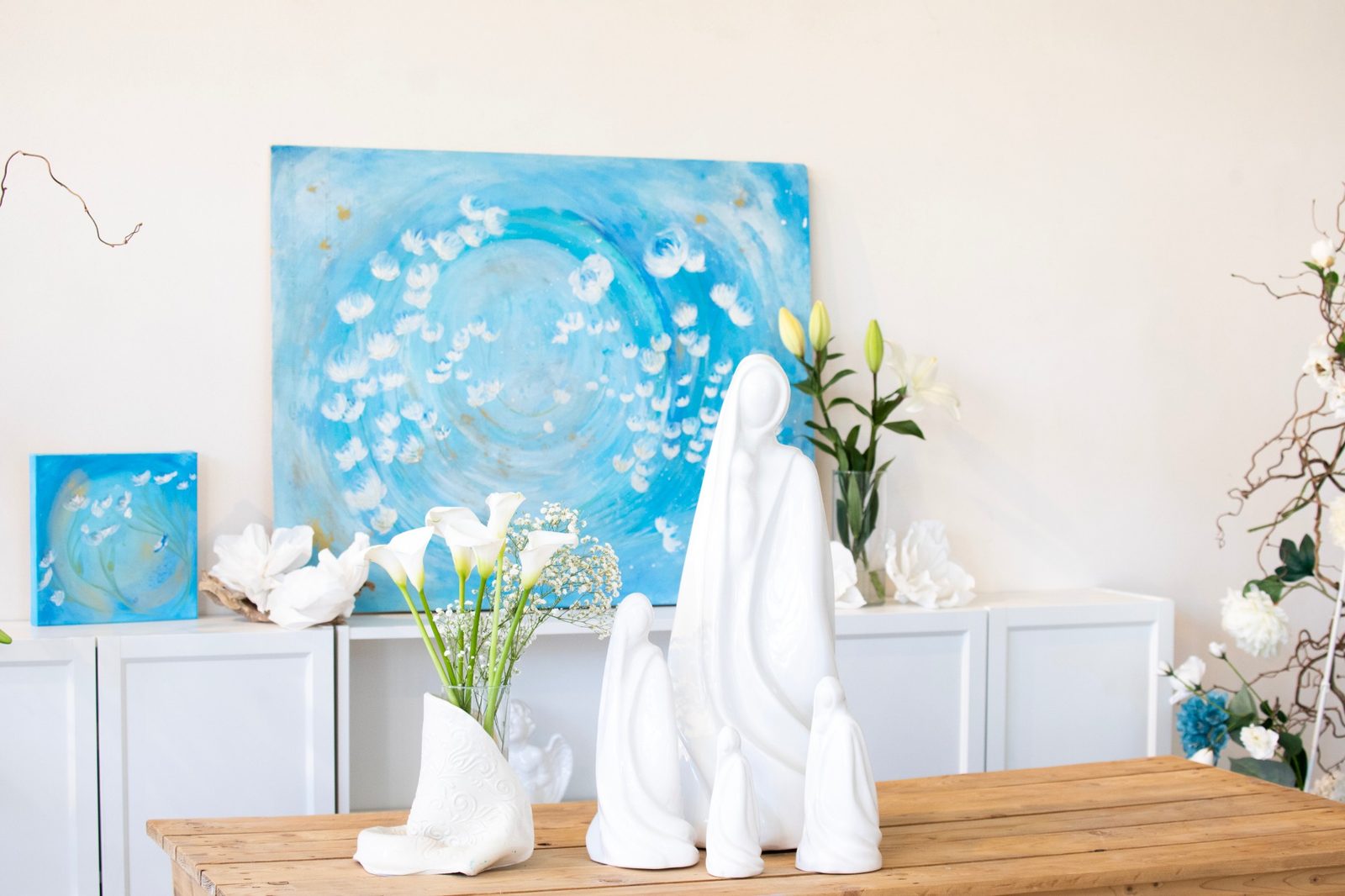 Dipinto azzurro con fiori bianchi e sculture in ceramica su un tavolo in legno