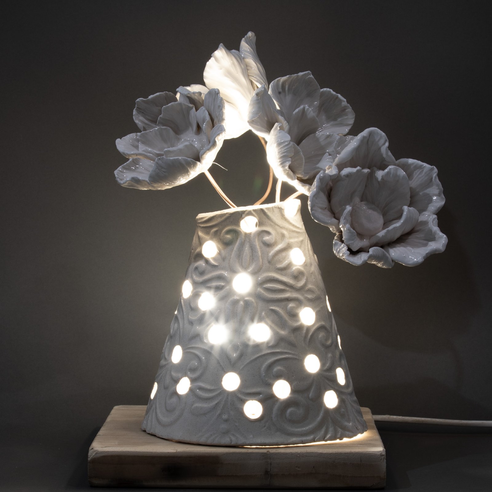 Lampada in ceramica traforata accesa, la luce filtra dalla materia