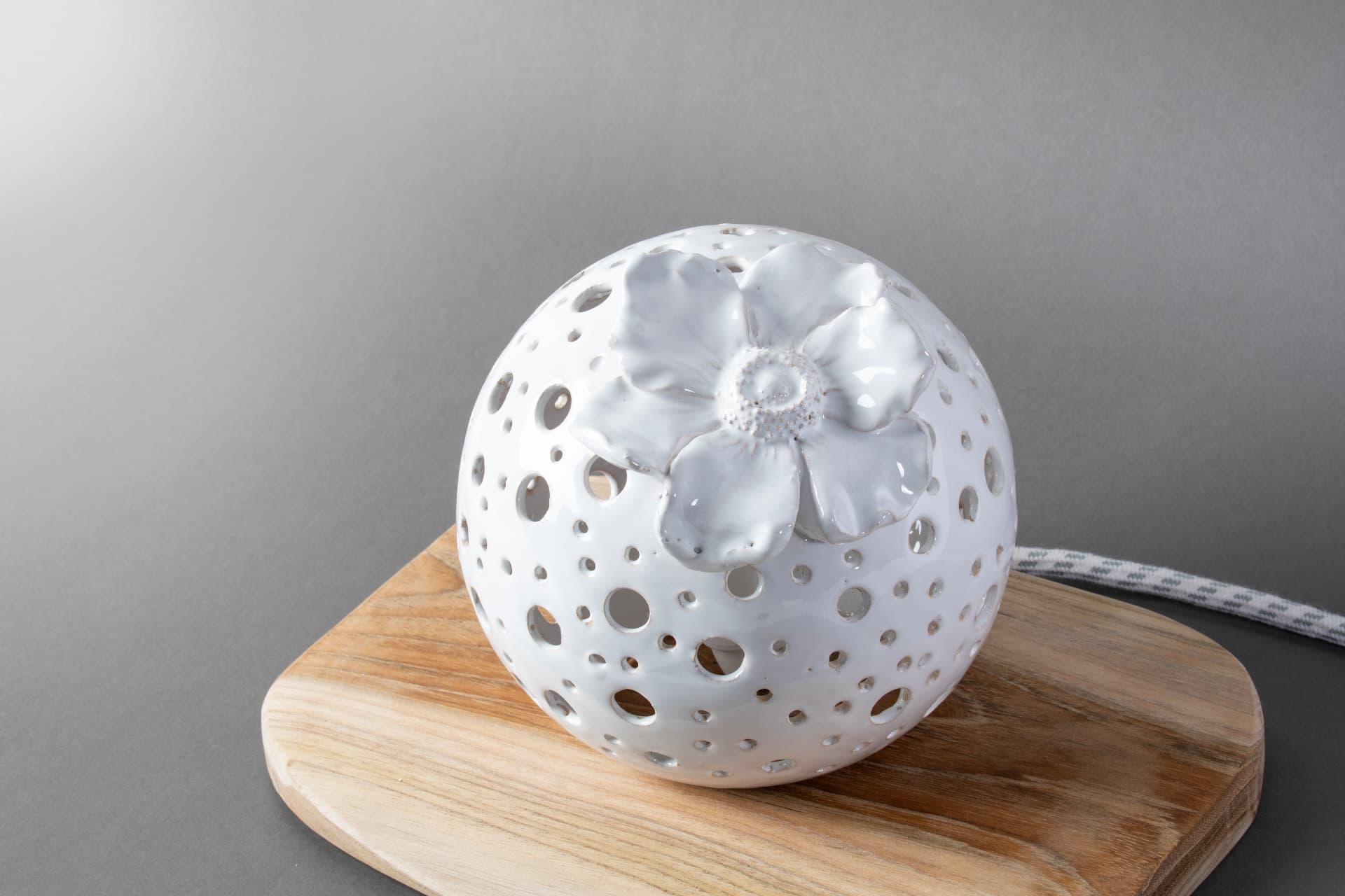 Lampada sfera in ceramica bianca traforata con fiore, illuminata nel buio